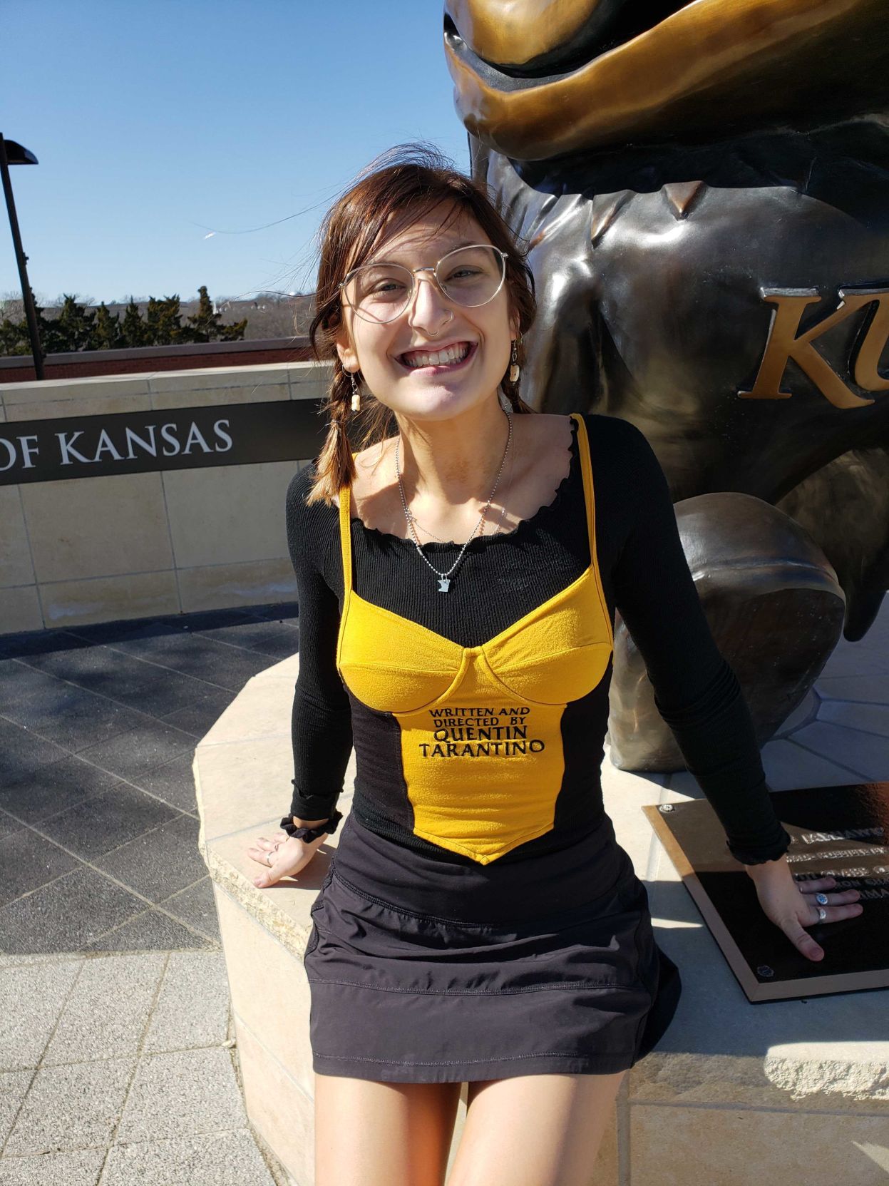 A woman sits next to a bronze Jayhawk statue